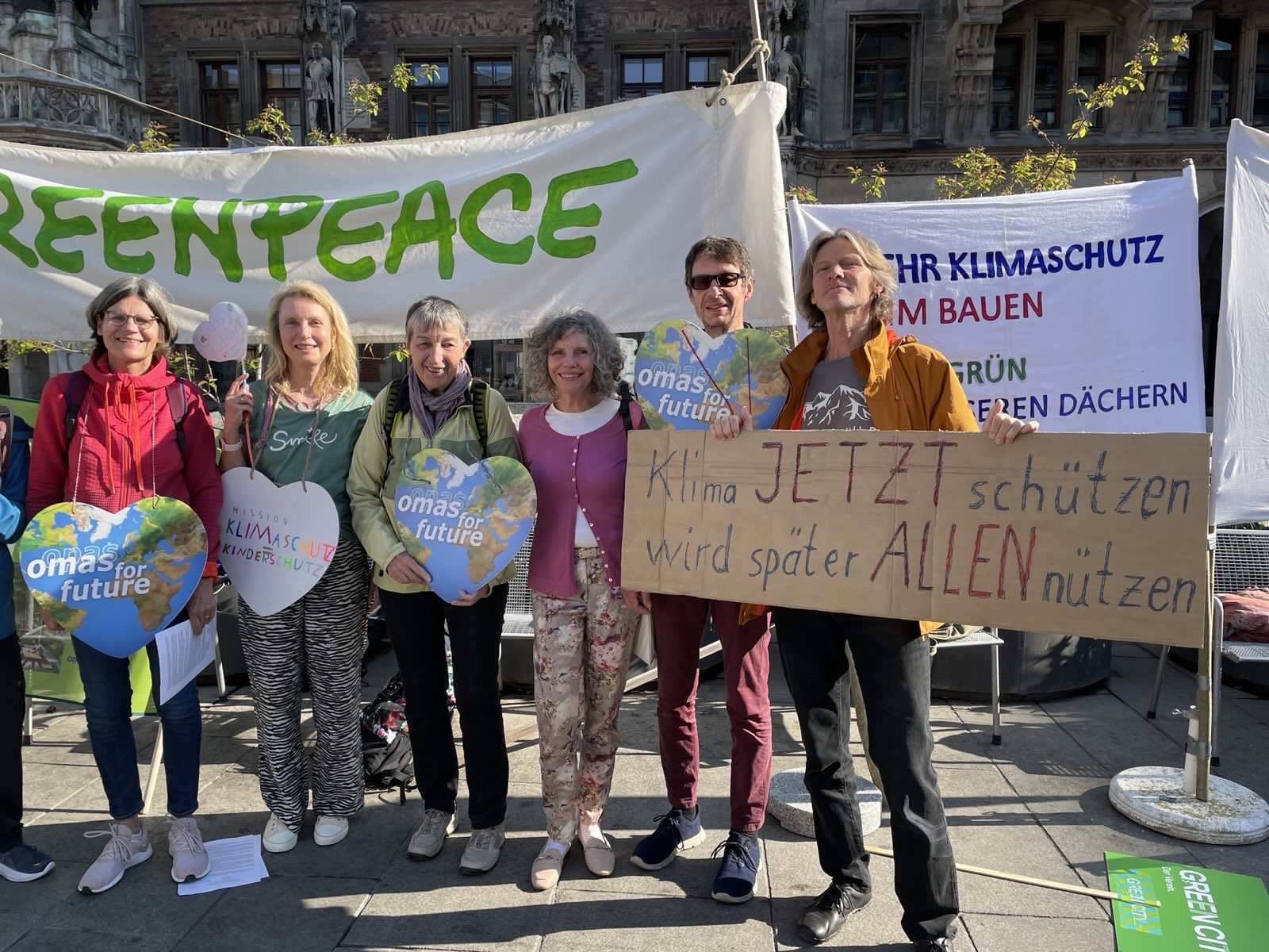 Sechs Personen stehen bei einer Klimaprotestaktion in Bad Kreuznach zusammen, halten Schilder und ein Greenpeace-Transparent. Auf einem Schild steht: "Klima JETZT schützen wird später ALLEN nützen". Die Gruppe lächelt und posiert im Freien.