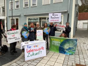 Eine Gruppe von Menschen steht draußen und hält Schilder in deutscher Sprache für Klimaschutz, Demokratie und eine lebenswerte Zukunft. Sie scheinen an einer friedlichen Protest- oder Sensibilisierungsveranstaltung teilzunehmen.